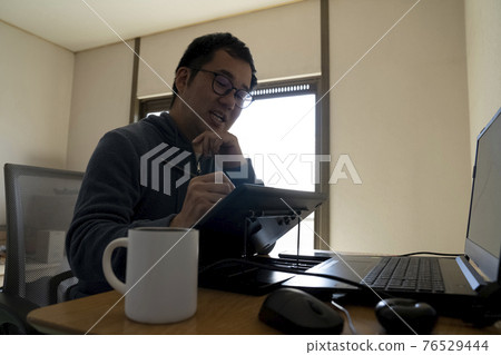 A man drawing an illustration with a pen tab 76529444