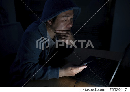 A man looking at a computer and smartphone at night A man looking at a computer and smartphone at night 76529447
