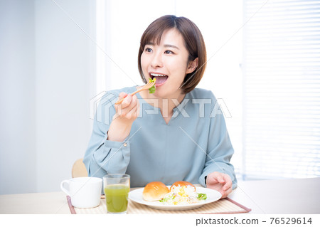 一個女人在陽光明媚的桌子上吃早餐 76529614