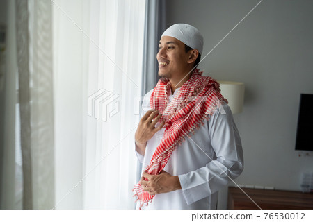 muslim asian man standing near window get dressed before going to the mosque 76530012