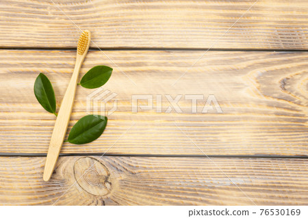 Natural eco friendly bamboo toothbrush with green tree leaves on a wooden background. Choose a wooden toothbrush. Recycling concept, no waste, no plastic, top view 76530169