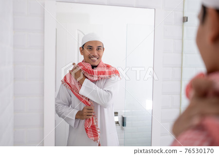 muslim man looking at mirror and get dressed before going to the mosque 76530170