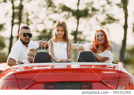Family in a cabriolet convertible car at the sunset 76533269