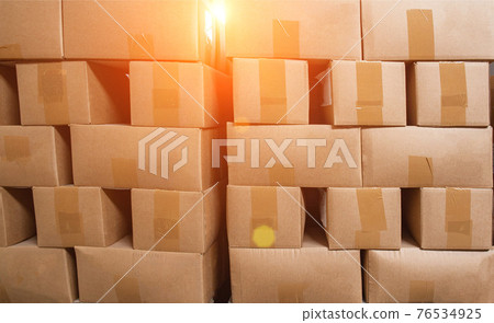 A pile of cardboard boxes on pallets against the backdrop of the sun. The concept of turnover, production, industry. Copy space 76534925