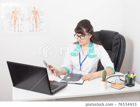A beautiful caucasian girl doctor in glasses makes a diagnosis based on the results of the examination of the patient. Decoding of blood tests, X-ray and ultrasound diagnostics. A beautiful caucasian girl doctor in glasses makes a diagnosis based on the results of the examination of the patient. Decoding of blood tests, X-ray and ultrasound diagnostics. 76534933