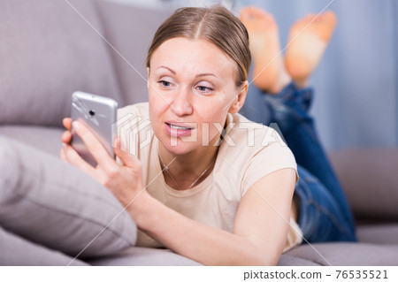 Woman looking at phone on sofa Woman looking at phone on sofa 76535521