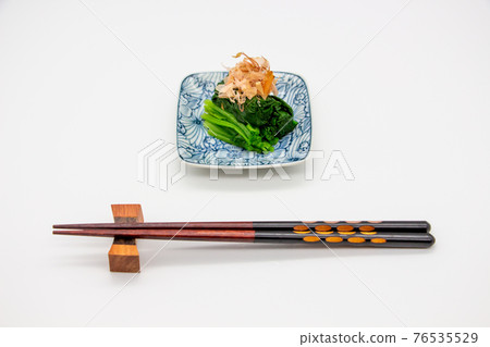 A set of chopsticks served with soaked spinach served on a small plate 76535529