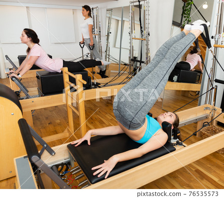 Woman exercising torson rotation at gym using pilates beds 76535573