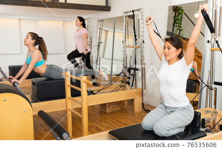Sportswoman stretching body on pilates chair while doing forward bends during workout Sportswoman stretching body on pilates chair while doing forward bends during workout 76535606