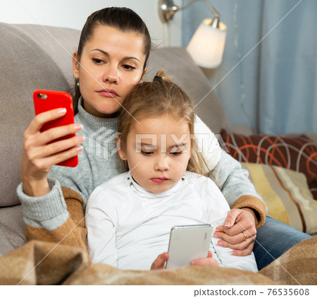 Young woman with small daughter looking at phone Young woman with small daughter looking at phone 76535608