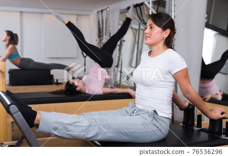 Hispanic girl doing pilates on reformer in fitness studio 76536296