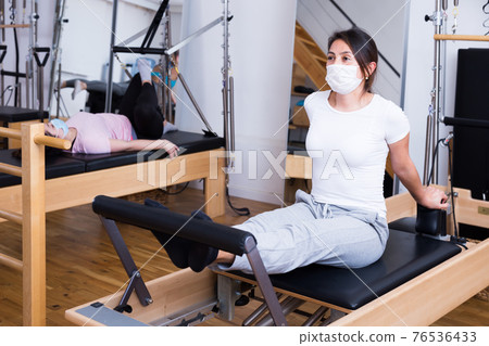 Hispanic girl in protective mask doing exercises on pilates reformer Hispanic girl in protective mask doing exercises on pilates reformer 76536433
