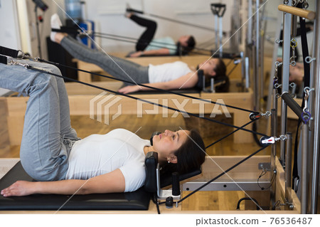 Young Hispanic woman performing pilates on reformer in fitness studio Young Hispanic woman performing pilates on reformer in fitness studio 76536487