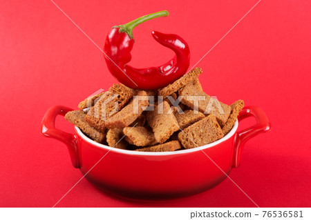 in a red pan are croutons with spices, a pod of red pepper lies on top, the concept of spicy food, on a red background 76536581