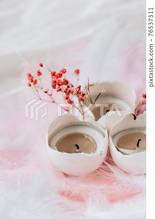 Composition of White egg shell with candle inside. Bright easter decorations with bird feathers. Pastel colors. Easter greeting card. 76537311