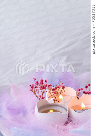 Composition of White egg shell with candle inside. Candle light. Bright easter decorations with bird feathers. Pastel colors. Easter greeting card. Composition of White egg shell with candle inside. Candle light. Bright easter decorations with bird feathers. Pastel colors. Easter greeting card. 76537313