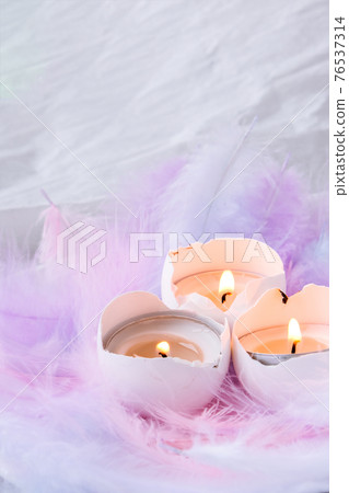 Composition of White egg shell with candle inside. Candle light. Bright easter decorations with bird feathers. Pastel colors. Easter greeting card. Composition of White egg shell with candle inside. Candle light. Bright easter decorations with bird feathers. Pastel colors. Easter greeting card. 76537314