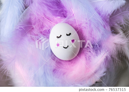 Funny smiley painted egg face in bird feather. Easter decorations. Copy space for text. Pastel colors. Easter greeting card. Funny smiley painted egg face in bird feather. Easter decorations. Copy space for text. Pastel colors. Easter greeting card. 76537315