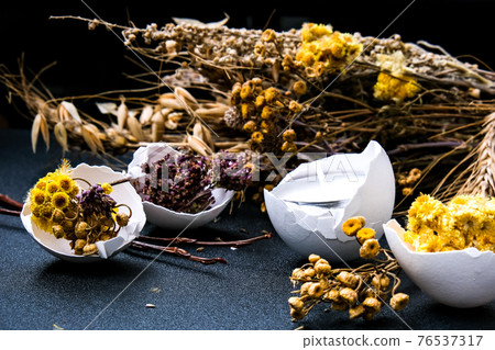 Trendy Easter decorations. Cracked organic eggs with dry grass and dry flowers candle on plate. Bird feather. Copy space. Greeting card. Dark background. Trendy Easter decorations. Cracked organic eggs with dry grass and dry flowers candle on plate. Bird feather. Copy space. Greeting card. Dark background. 76537317