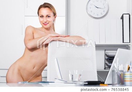 Young nude woman standing near the table and posing in the office Young nude woman standing near the table and posing in the office 76538845