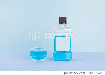 Bottle and glass of mouthwash for oral hygiene routine on light blue background. Mouth rinse liquids help to against bad breath, cavities and plaque. Dental care product. Bottle and glass of mouthwash for oral hygiene routine on light blue background. Mouth rinse liquids help to against bad breath, cavities and plaque. Dental care product. 76539521