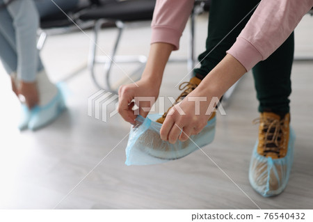 People in line put on protective shoe covers People in line put on protective shoe covers 76540432