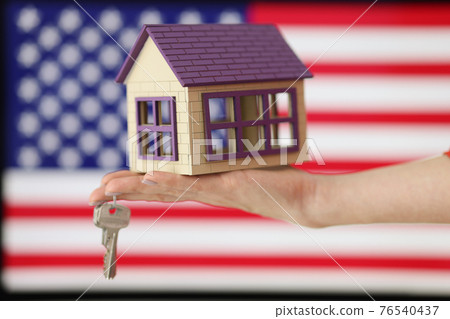 Small house with keys on hand against background of American flag Small house with keys on hand against background of American flag 76540437