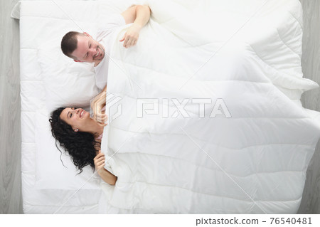 Laughing man and woman on large white bed 76540481
