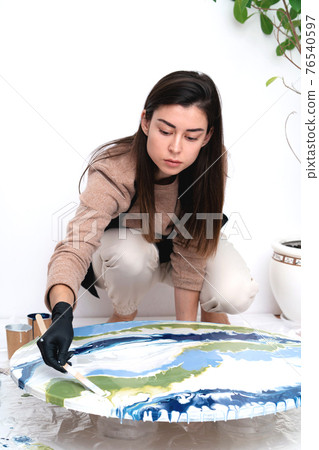 A young woman creates a painting using liquid art technique 76540597