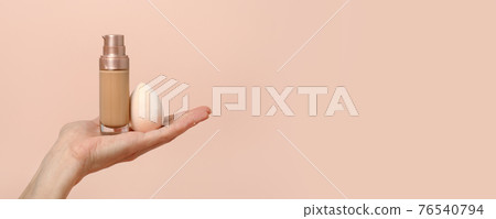 Applying foundation on makeup sponge. Woman's hands with neutral manicure holding bottle of concealer or toner foundation, cream and beauty blender, make up artist background, banner, flyer 76540794