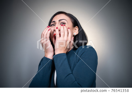 studio shot of scared or afraid brunette female on grey background 76541358