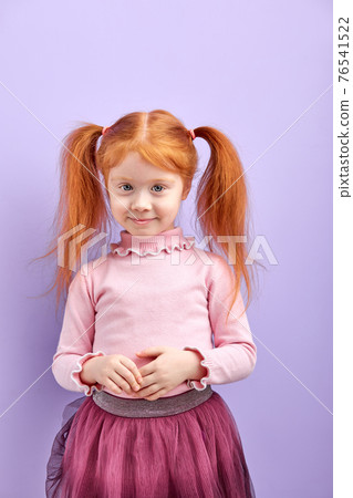 Shy diligent redhead kid girl with two pony tails posing at camera, smiling 76541522