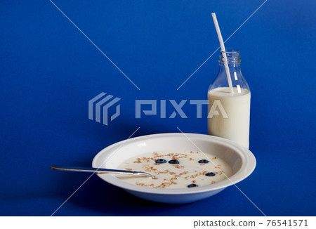 Closeup composition of fresh milk and a plate of muesli with berries, isolated on blue background Closeup composition of fresh milk and a plate of muesli with berries, isolated on blue background 76541571