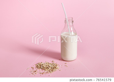 Close-up view of glass bottle with milk and oat flakes on pink background with space for text 76541579