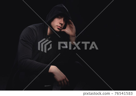 Studio portrait of a man in a hood, a shadow hides his face. Anonymity shadow economy and evasion from the law 76541583