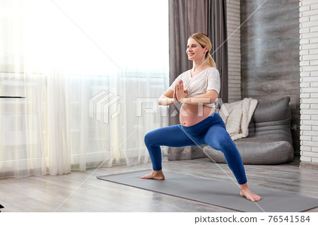 Happy pregnant caucasian woman training yoga at home 76541584