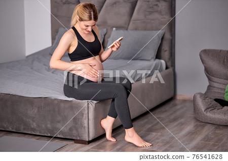 Side view on pretty pregnant woman sitting with mobile phone, having rest 76541628