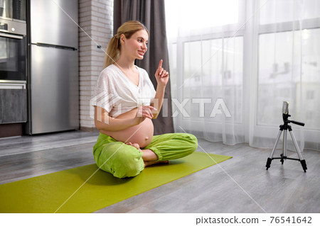 Young beautiful pleasant lady recording video online translation on mobile phone showing yoga exercises Young beautiful pleasant lady recording video online translation on mobile phone showing yoga exercises 76541642