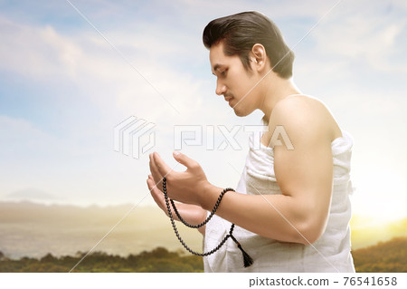 Asian Muslim man in ihram clothes praying with prayer beads on his hands 76541658
