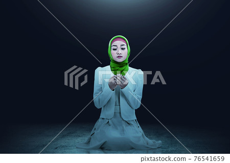 Asian Muslim woman in a veil sitting while raised hands and praying 76541659