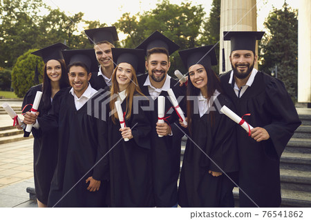 Group of happy graduates walking with dimplomas in raised hands over university building background Group of happy graduates walking with dimplomas in raised hands over university building background 76541862
