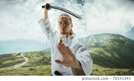 Young man, teacher fighting Aikido, training martial arts on meadow in front mountains Young man, teacher fighting Aikido, training martial arts on meadow in front mountains 76541943