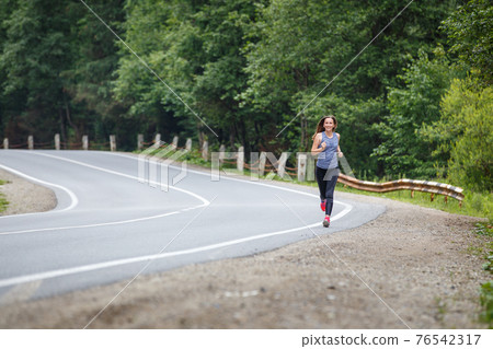 Young slim woman running on the road in summer Young slim woman running on the road in summer 76542317