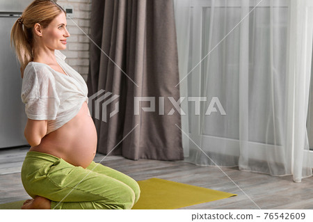 side view on pregnant woman stretching body at home, going to do yoga exercises on floor side view on pregnant woman stretching body at home, going to do yoga exercises on floor 76542609