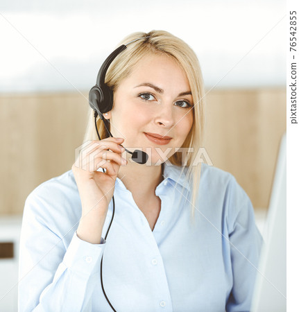 Blonde business woman sitting and communicated by headset in call center office. Concept of telesales business or home office occupation 76542855