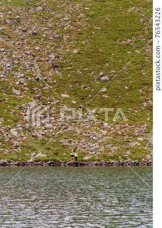 A couple of tourists stand on the edge of a mountain lake, Lake Brebeneskul, the Montenegrin ridge, the Carpathians of Ukraine. 76543226