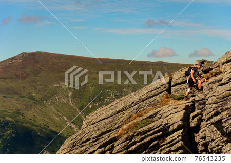 traveler, tourist, traveler stands on top of a cliff and enjoys a sunny day and a view of the picturesque Carpathians. 76543235