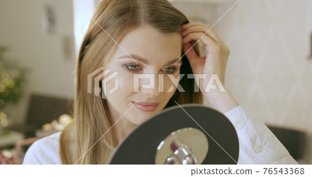 A young woman looks in the mirror, preens herself, admires herself, straightening her clothes and hairstyle. Smiles and likes herself. Start to new day, enjoying morning. Beauty salon makeup A young woman looks in the mirror, preens herself, admires herself, straightening her clothes and hairstyle. Smiles and likes herself. Start to new day, enjoying morning. Beauty salon makeup 76543368