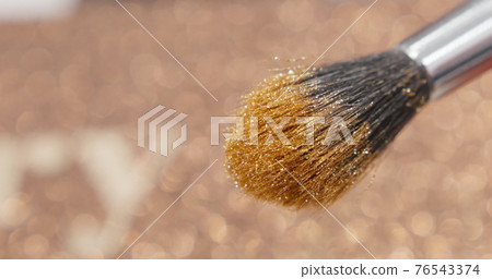 Brush gains glitter to be used in make-up. Macro view of working process, tools in beauty industry. Fashion glamour shiny glitter concept. 76543374