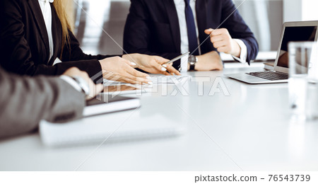 Unknown businessmen and woman sitting, working and discussing questions at meeting in modern office, close-up 76543739